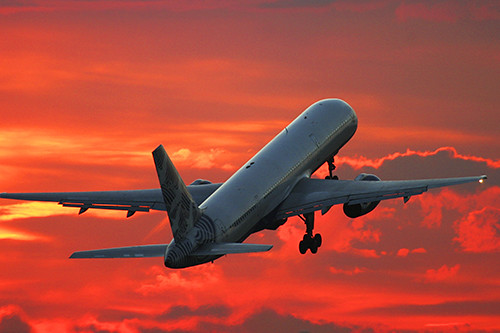 A flight flying high with an orange coloured sky in the background.